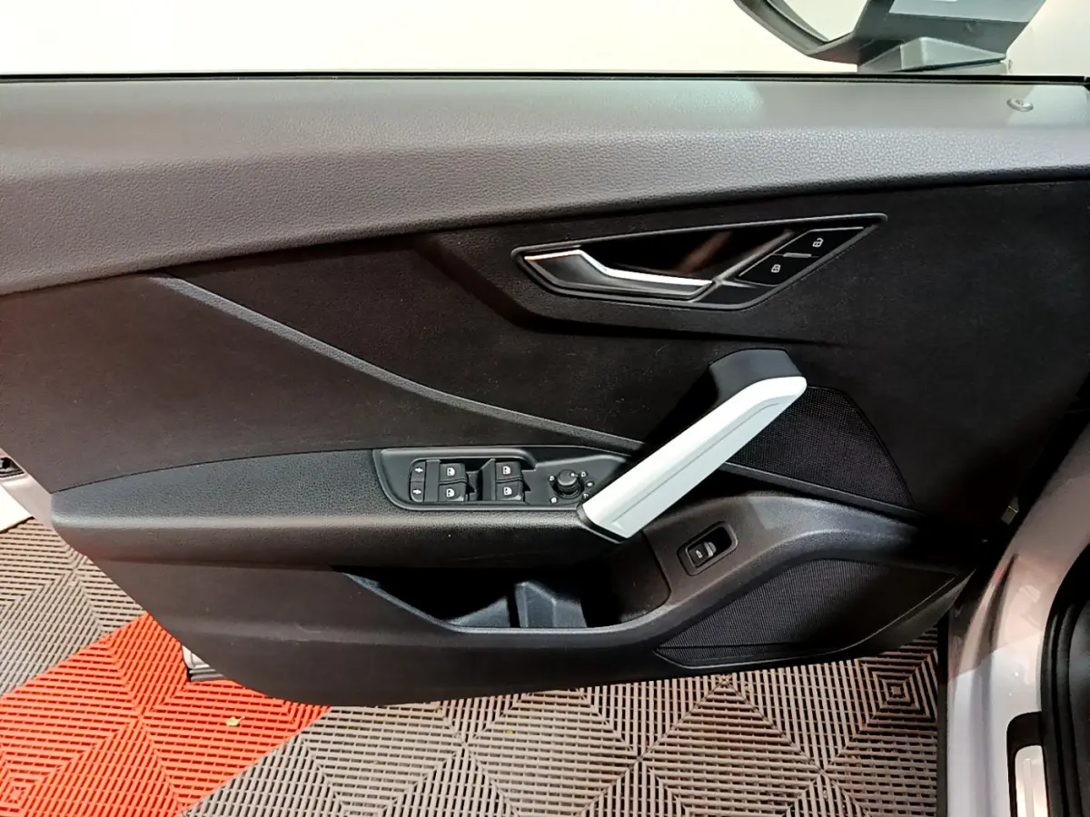 Vue intérieure du panneau de porte côté conducteur de l'Audi Q2 gris clair avec commandes de vitres et poignée argentée.