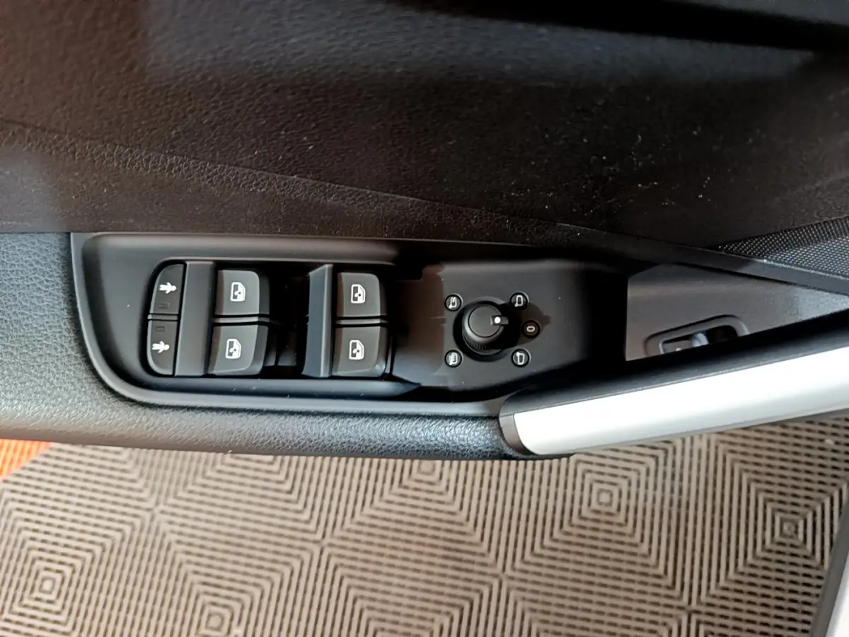 Gros plan sur les commandes de lève-vitres et réglage des rétroviseurs côté conducteur d’un Audi Q2 gris clair, intérieur noir.