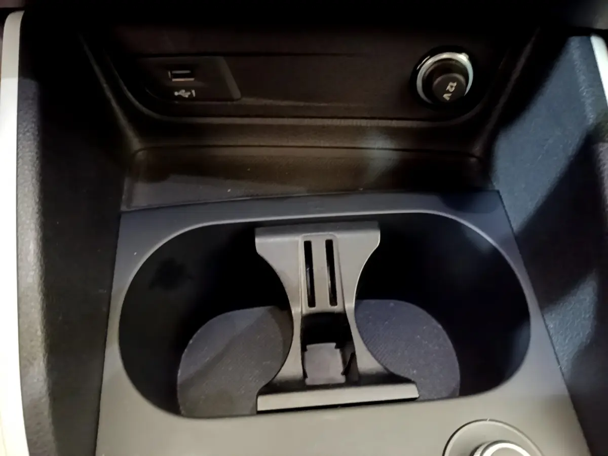 Gros plan sur les porte-gobelets centraux noirs de l’Audi Q2 35 TDI 150 Design gris clair, avec prise 12V visible.