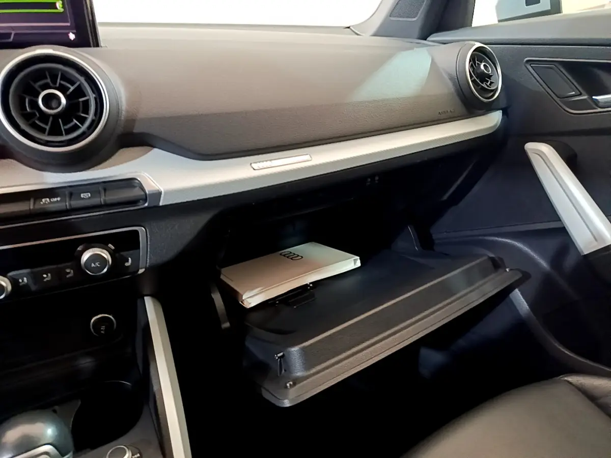 Intérieur de l'Audi Q2 35 TDI 150 Design 2020, vue côté passager sur la boîte à gants ouverte avec manuel Audi.