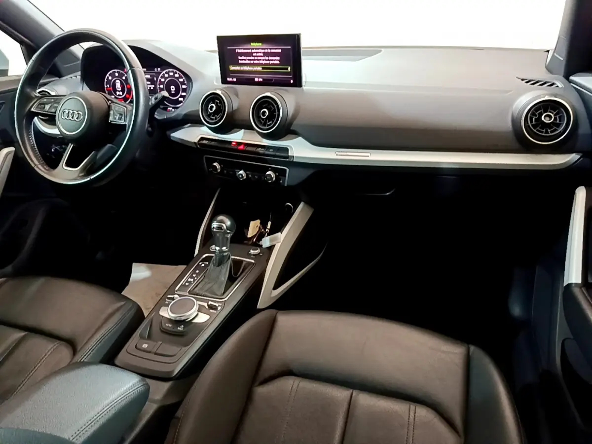 Intérieur Audi Q2 35 TDI 2020 vu côté conducteur, tableau de bord noir avec écran central et volant cuir multifonctions.