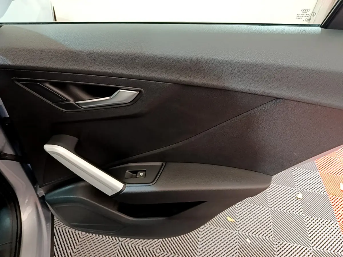 Vue intérieure du panneau de porte côté gauche de l'Audi Q2 35 TDI gris clair, avec poignée argentée et bouton de verrouillage.