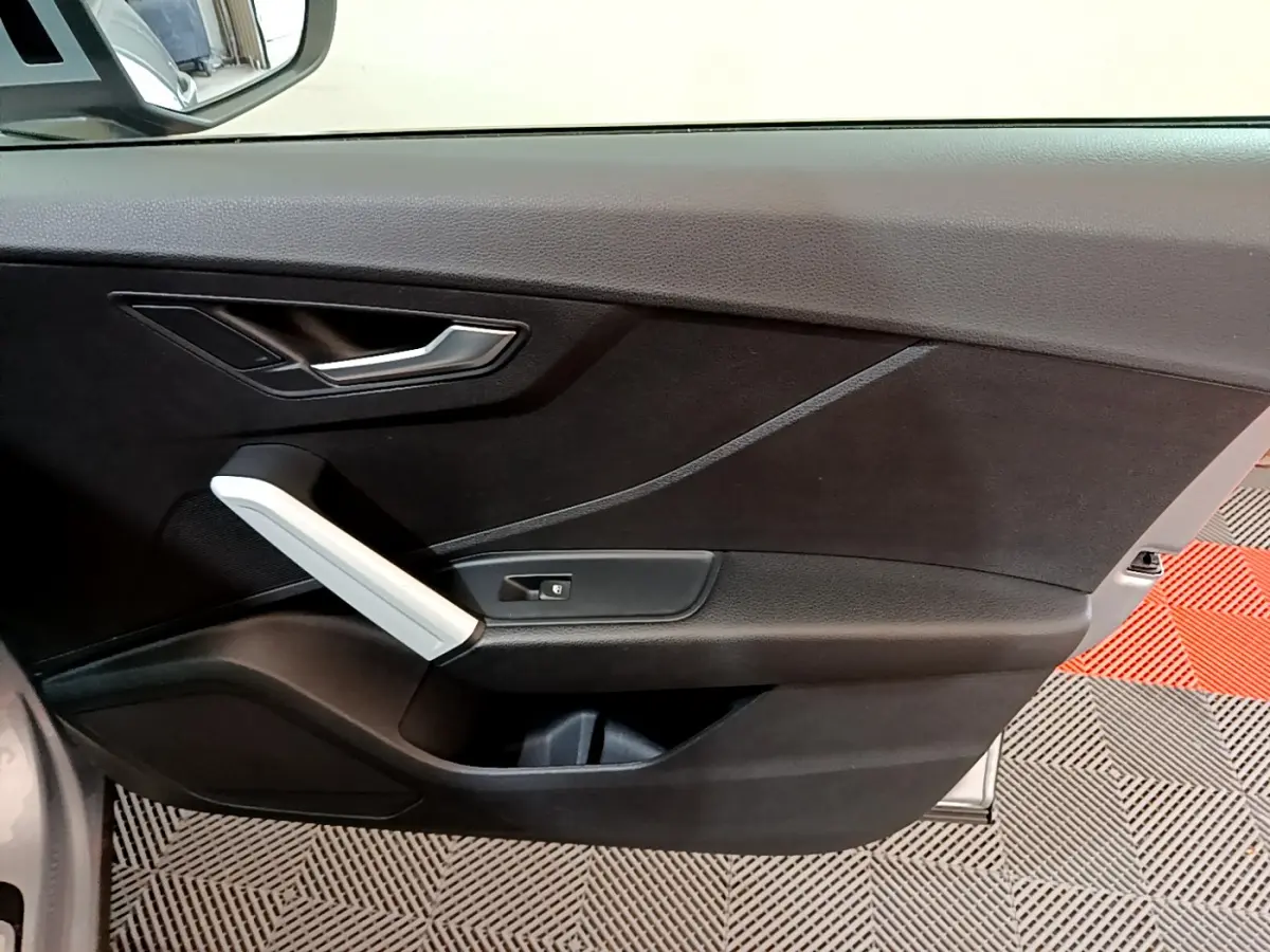 Vue intérieure du panneau de porte côté conducteur d'un Audi Q2 gris clair, avec poignée argentée et bouton de verrouillage.