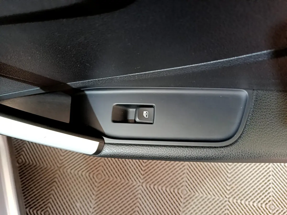 Bouton de commande de vitre électrique sur la porte côté conducteur d'un Audi Q2 gris clair, vue rapprochée.