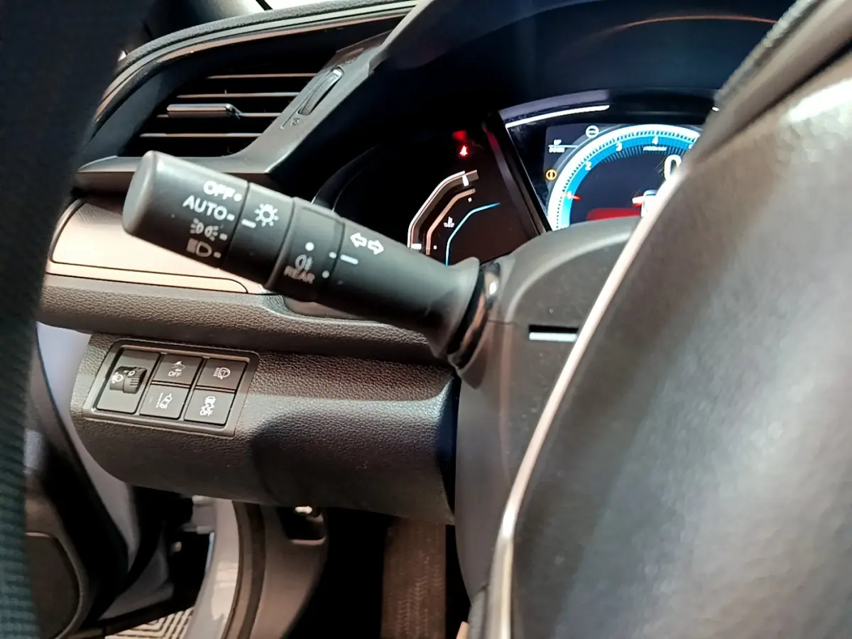 Vue rapprochée du commodo d'éclairage et du tableau de bord numérique de la Honda Civic 1.0 i-VTEC gris foncé.