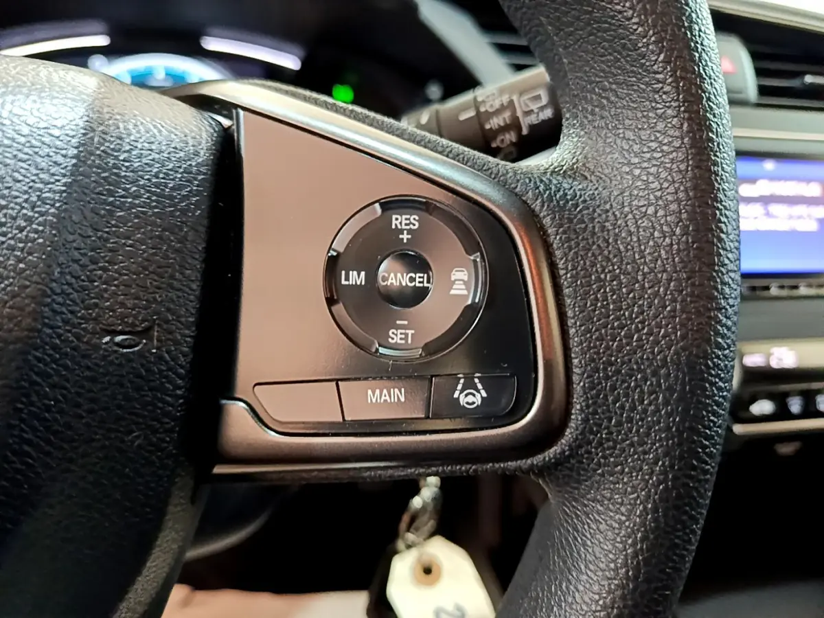 Gros plan sur les commandes du régulateur de vitesse au volant cuir noir d'une Honda Civic gris foncé 2020.