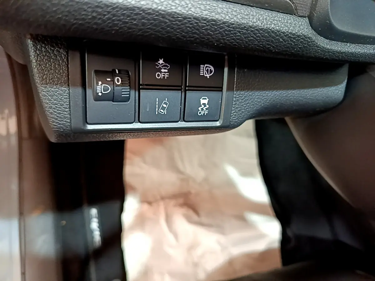 Boutons de réglage des phares et aides à la conduite sous le tableau de bord d'une Honda Civic 1.0 i-VTEC Exclusive gris foncé de 2020.