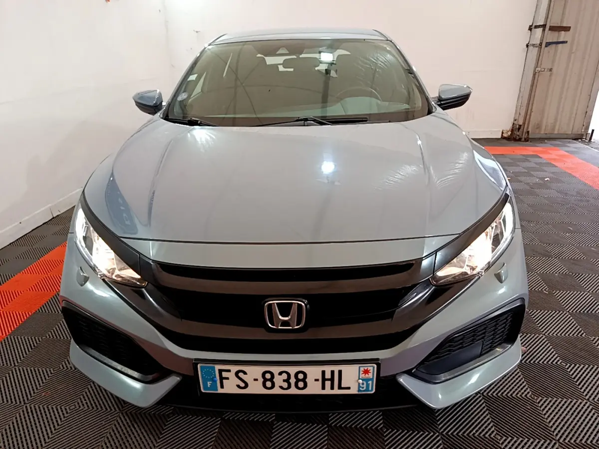 Vue frontale d'une Honda Civic gris foncé 2020 avec phares allumés et calandre noire brillante.