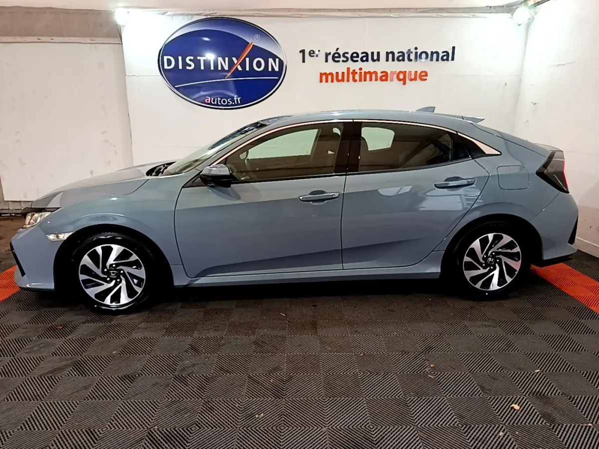 Profil côté gauche d'une Honda Civic 1.0 i-VTEC Exclusive gris foncé, avec jantes alliage et vitres teintées, en intérieur showroom.