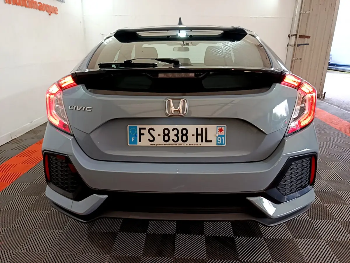 Vue arrière d'une Honda Civic gris foncé 2020 avec feux arrière allumés et aileron noir distinctif.