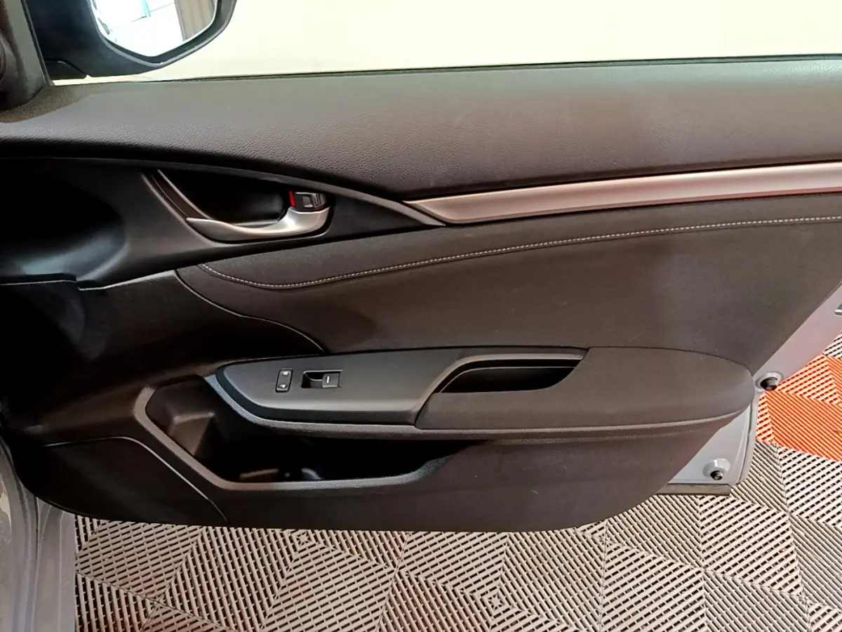 Vue intérieure du panneau de porte côté droit de la Honda Civic 1.0 i-VTEC Exclusive gris foncé, avec poignée métallique et commandes vitres.