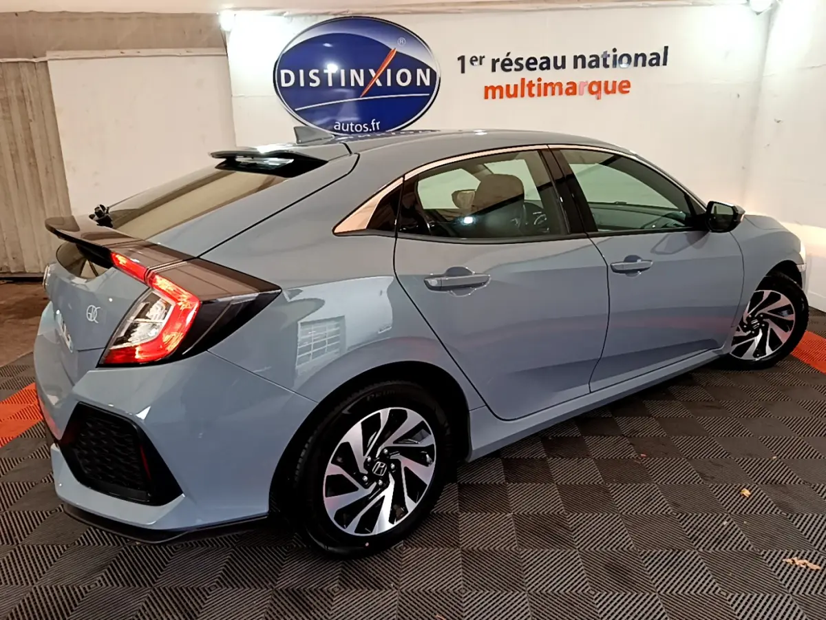 Vue 3/4 arrière droite d'une Honda Civic gris foncé 2020 avec jantes alliage et feux arrière allumés dans un showroom.