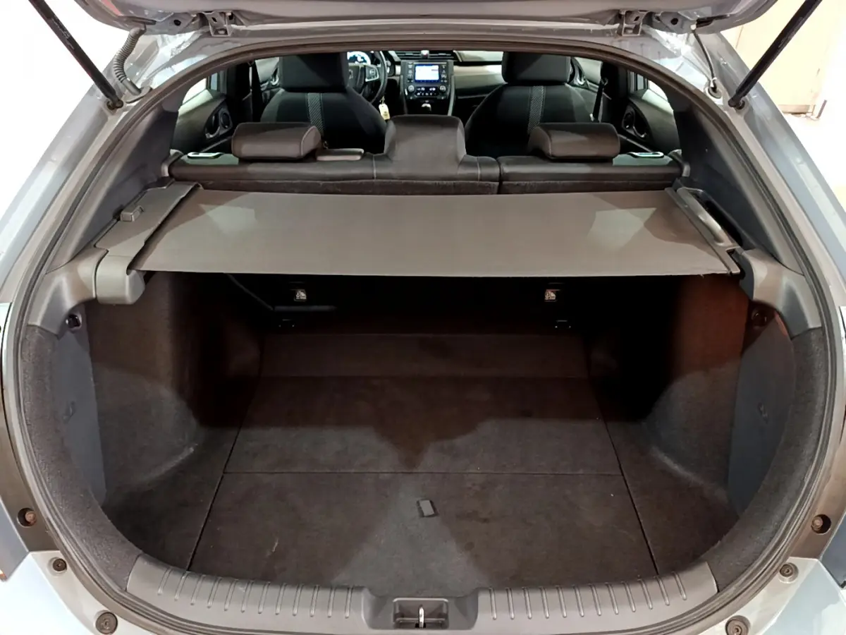Vue intérieure du coffre ouvert d'une Honda Civic gris foncé, avec tablette cache-bagages et sièges arrière visibles.