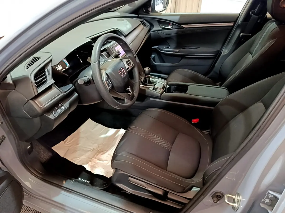 Vue intérieure côté conducteur de la Honda Civic 1.0 i-VTEC Exclusive 2020 avec sièges noirs et volant cuir multifonctions.