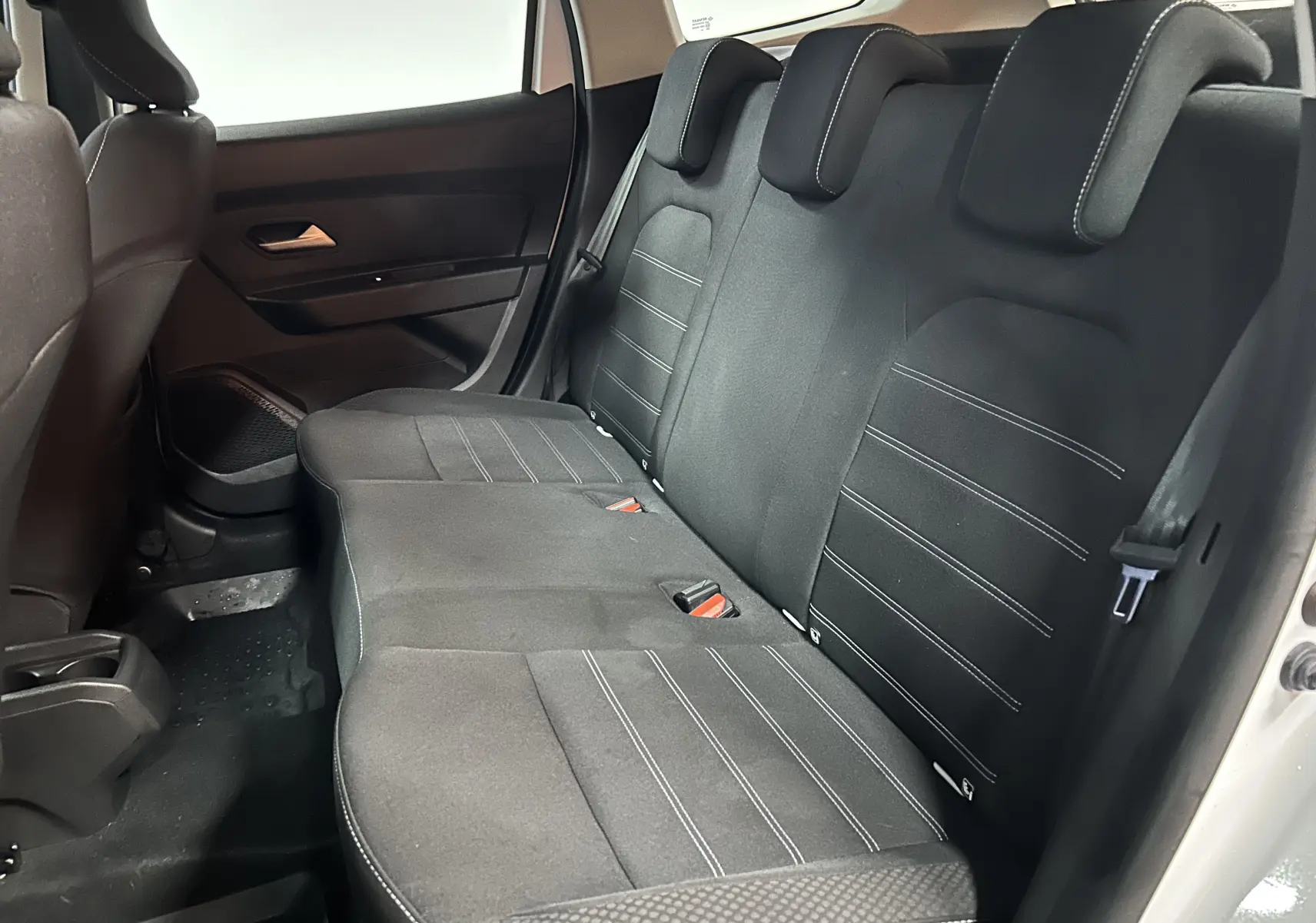 Vue intérieure côté droit des sièges arrière noirs en tissu du Dacia Duster blanc 2024, avec appuie-têtes et ceinture de sécurité visibles.