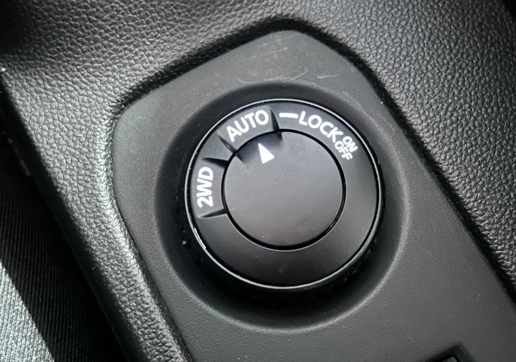 Gros plan sur le sélecteur de mode de traction 2WD, AUTO et LOCK dans l’habitacle noir du Dacia Duster blanc 2024.