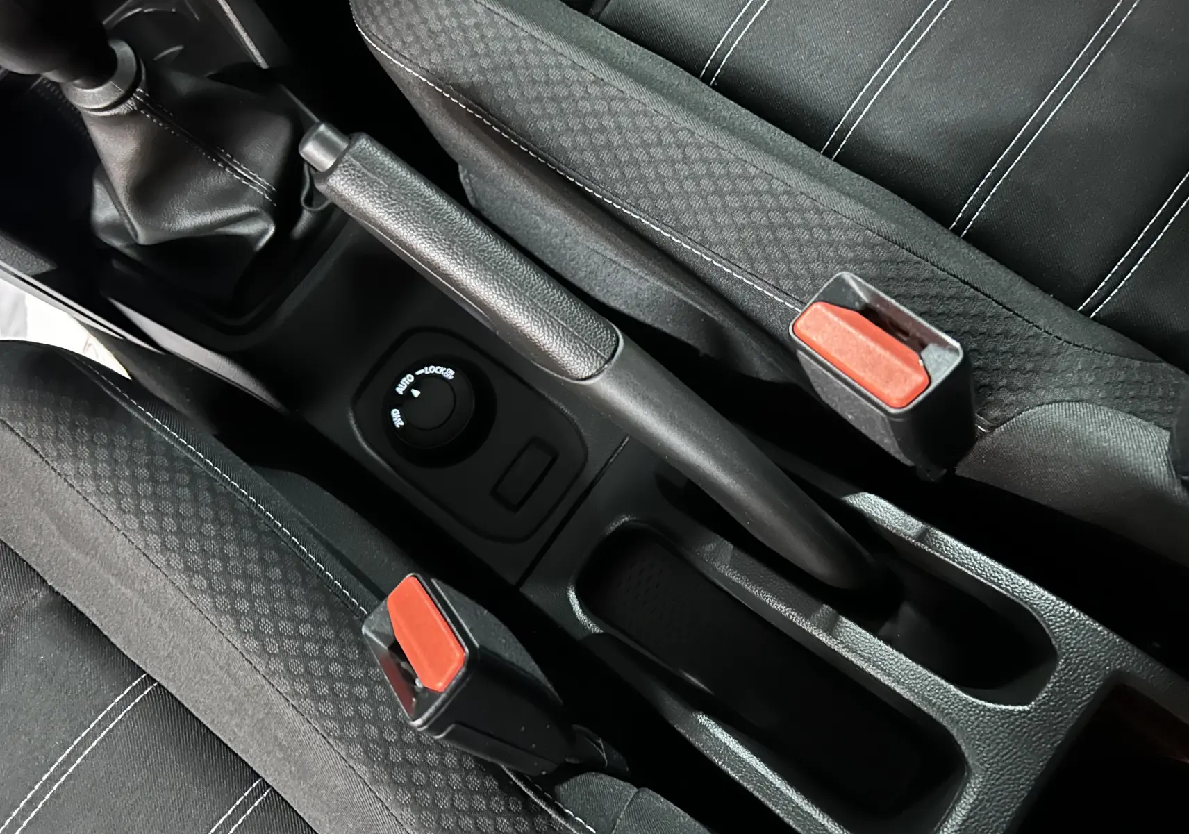 Vue rapprochée de la console centrale intérieure du Dacia Duster 2024, montrant frein à main et sièges tissu noirs.