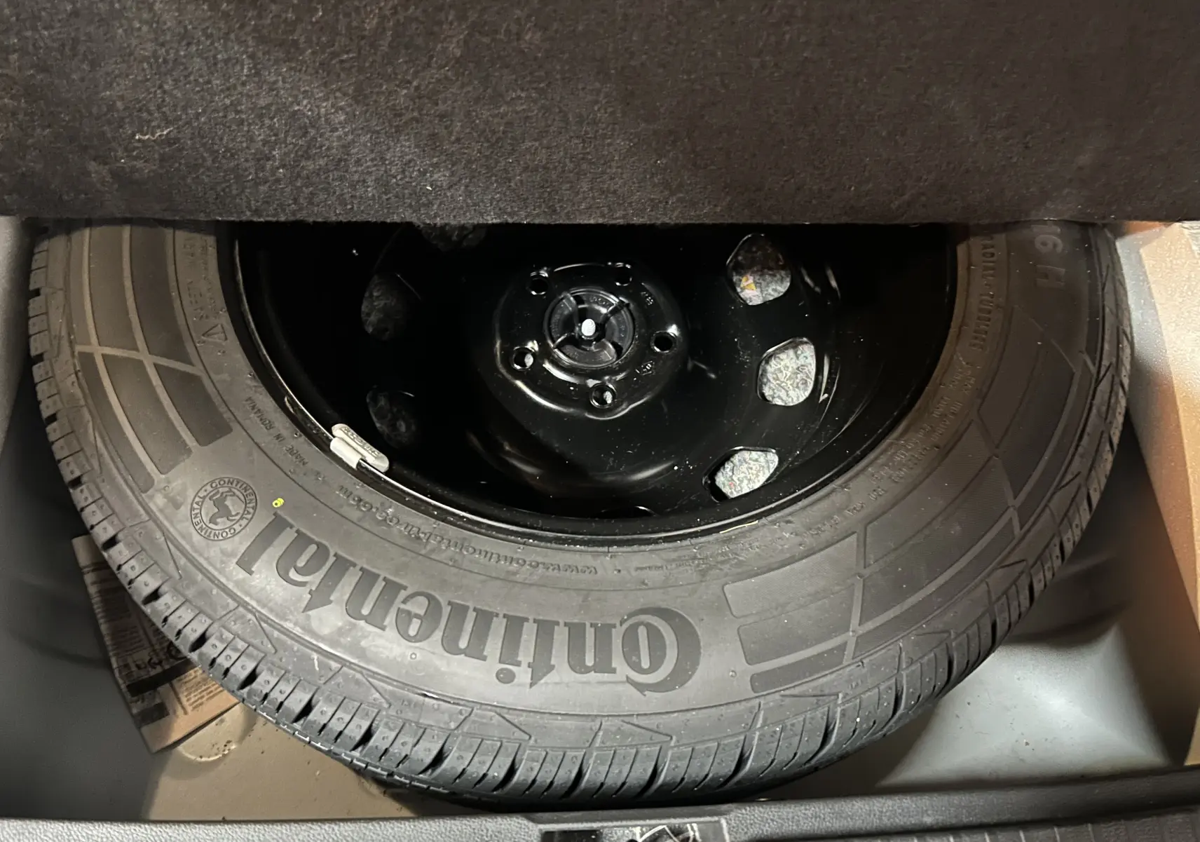 Gros plan sur la roue de secours Continental noire, logée dans le coffre du Dacia Duster blanc 2024.