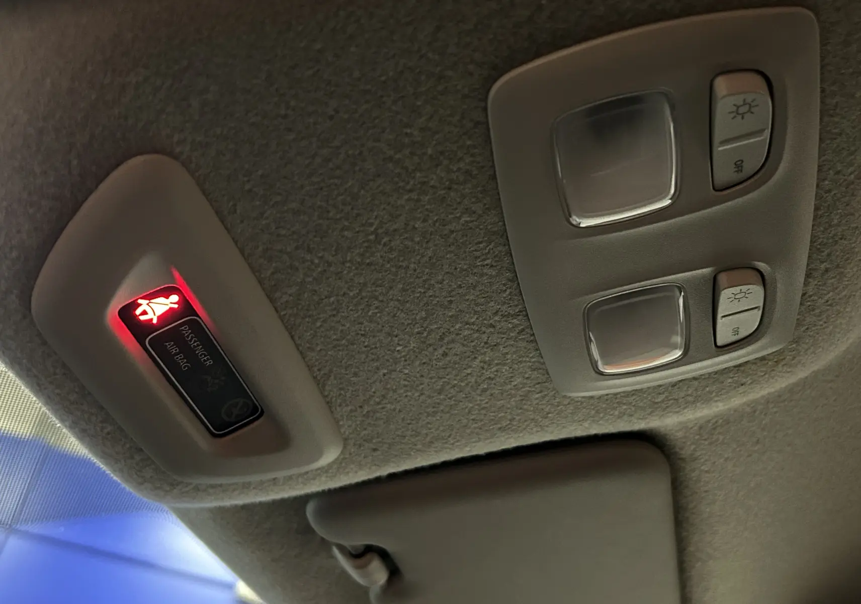 Détail du plafonnier intérieur avec témoin airbag passager allumé et commandes d’éclairage sur Dacia Duster blanc.