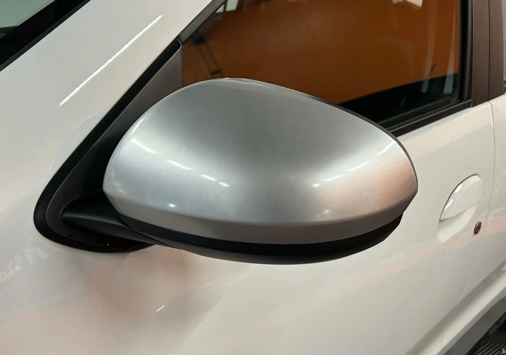 Rétroviseur côté gauche argenté sur Dacia Duster blanc 2024, vue rapprochée sur la portière avant.