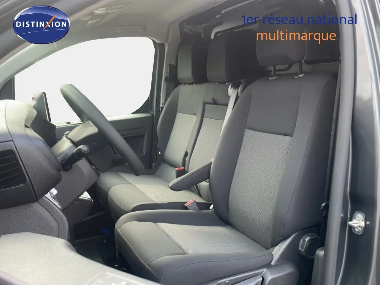 Vue intérieure côté conducteur du Citroën Jumpy gris titane, montrant les sièges avant en tissu gris et le volant multifonction.