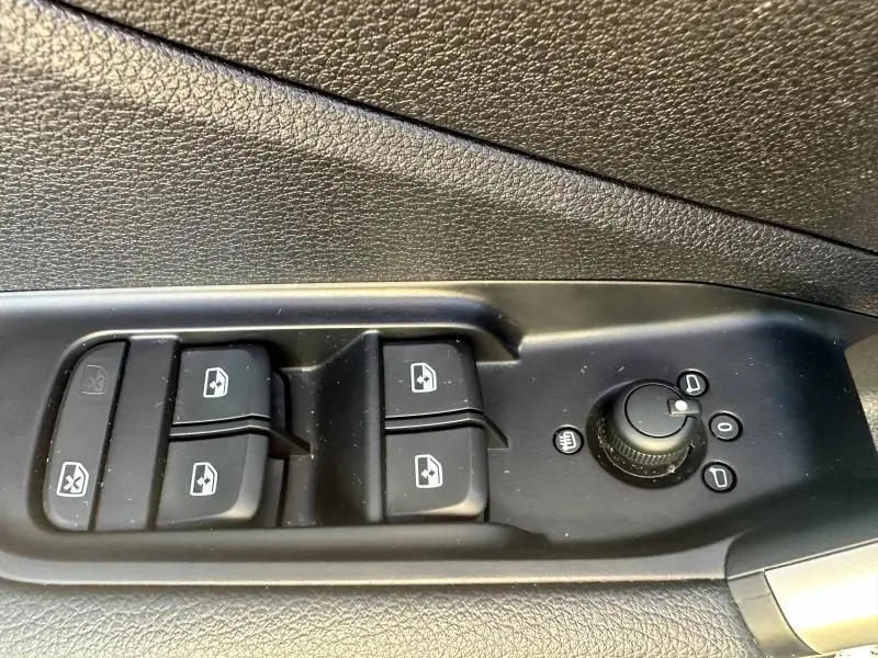 Gros plan sur les commandes de lève-vitres et réglage des rétroviseurs côté conducteur d’une Audi Q2 blanche.