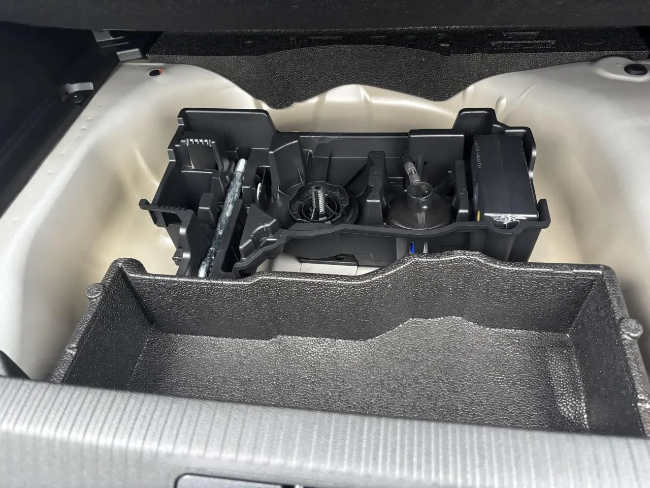 Coffre ouvert du Peugeot 2008 hybride 2025 montrant le rangement sous plancher avec outils et espace de rangement noir.