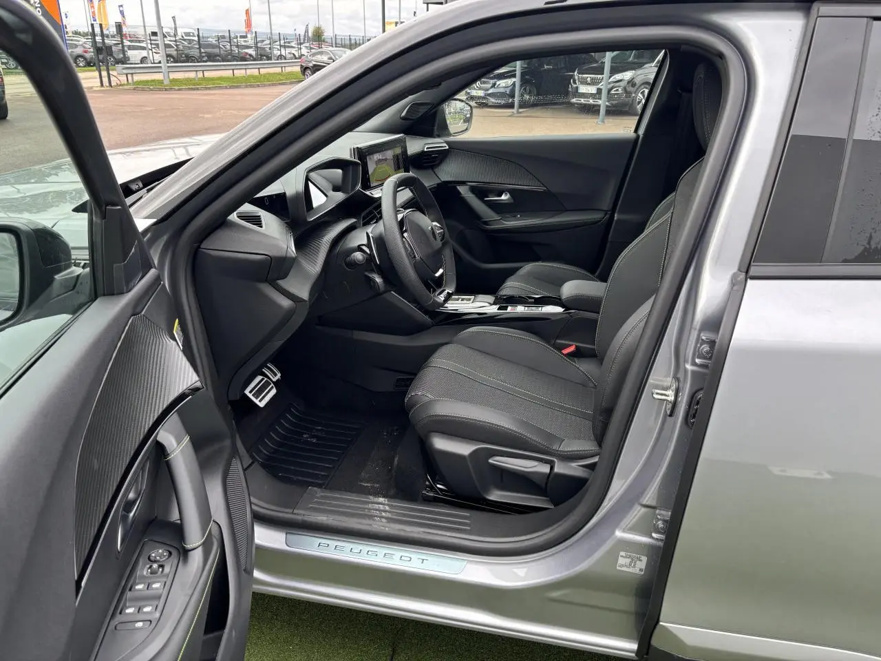 Vue intérieure côté conducteur du Peugeot 2008 gris Artense, mettant en valeur les sièges noirs et le tableau de bord moderne.