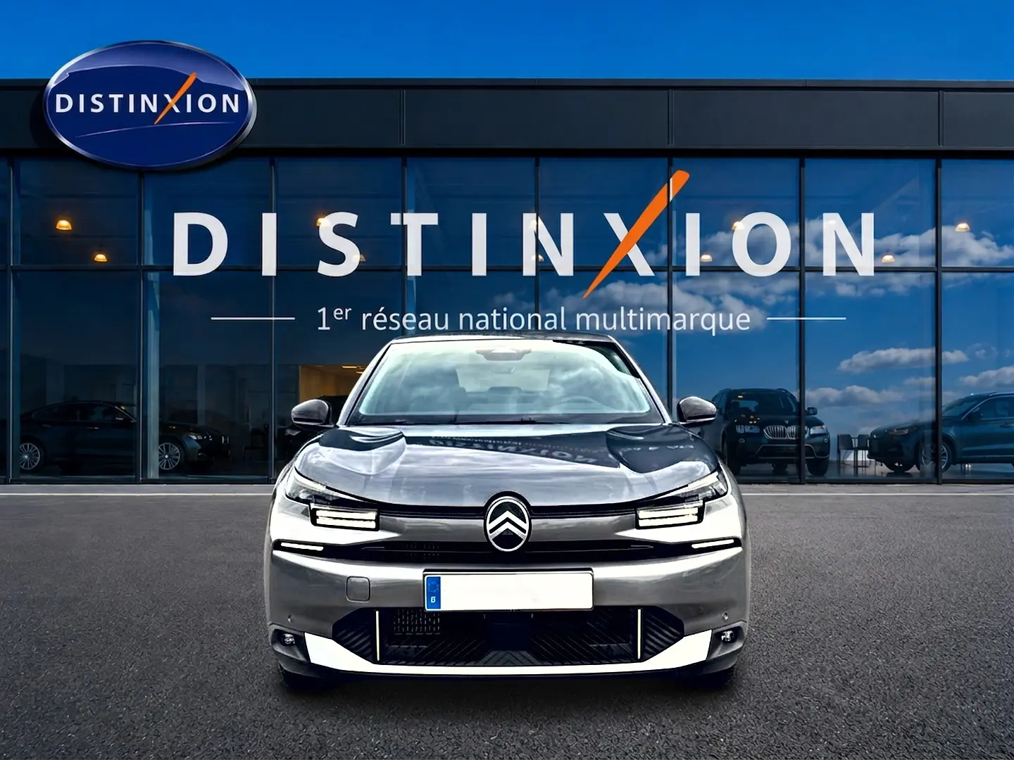 Vue de face d'une Citroën C4 X gris mercure stationnée devant une vitrine avec logo Distinxion.