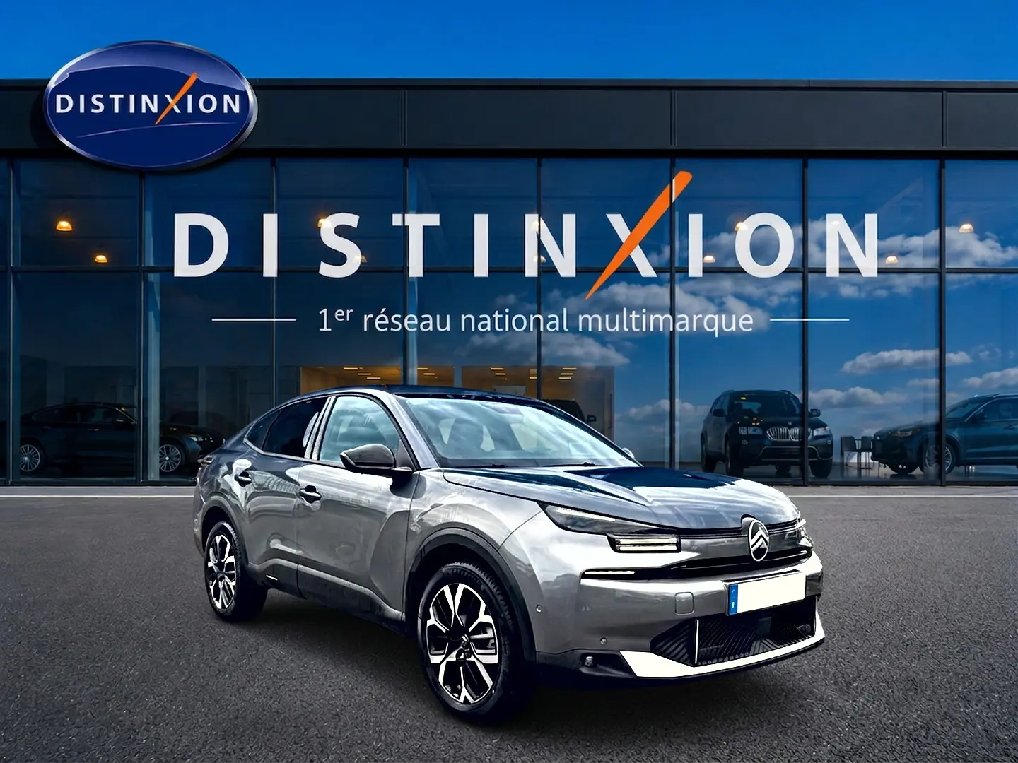 Citroën C4 X gris mercure vue 3/4 avant droit, avec jantes alu et calandre distinctive devant un showroom Distinxion.