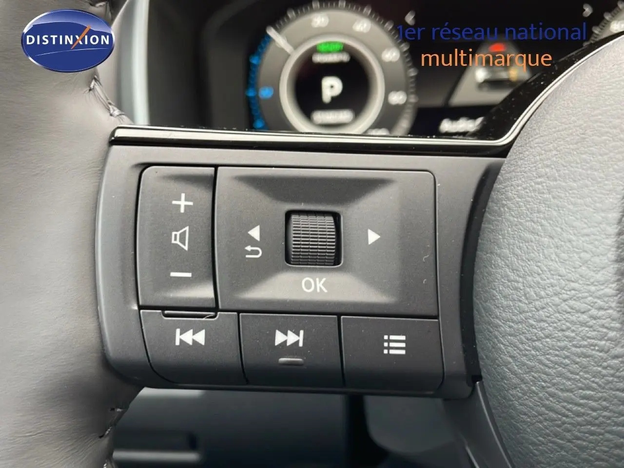 Gros plan sur les commandes multifonctions au volant du Nissan Qashqai gris, avec tableau de bord numérique en arrière-plan flou.