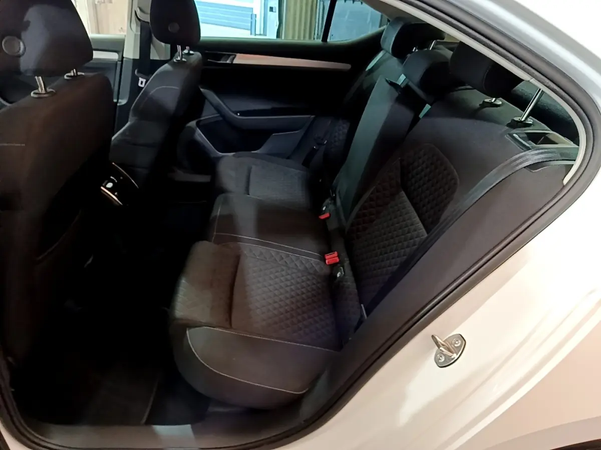 Vue intérieure côté droit sur la banquette arrière noire matelassée d’une Skoda Superb blanche, porte ouverte.