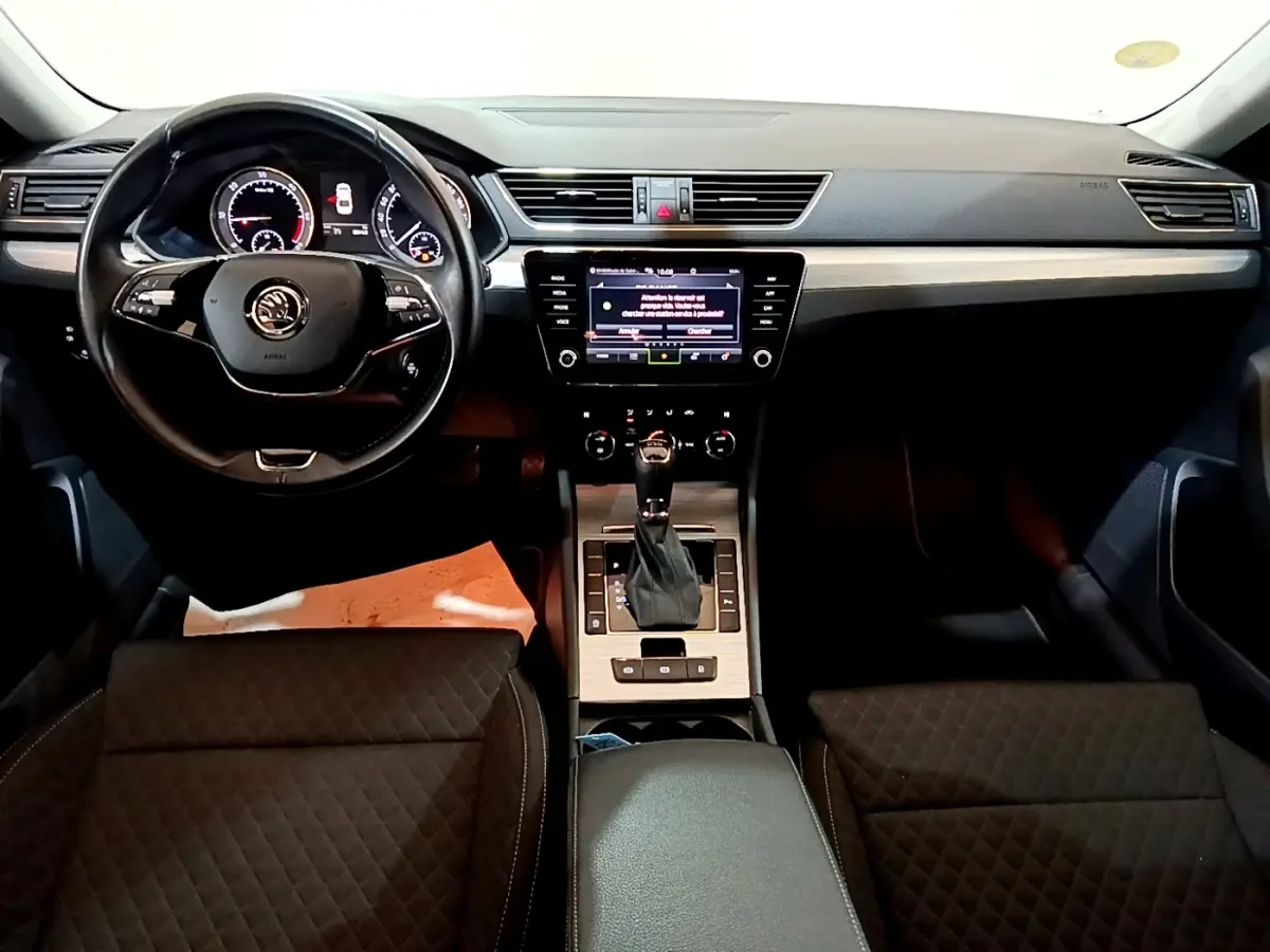 Vue intérieure avant centrée sur le tableau de bord et volant cuir noir de la Skoda Superb 2021 avec écran tactile et console bois clair.
