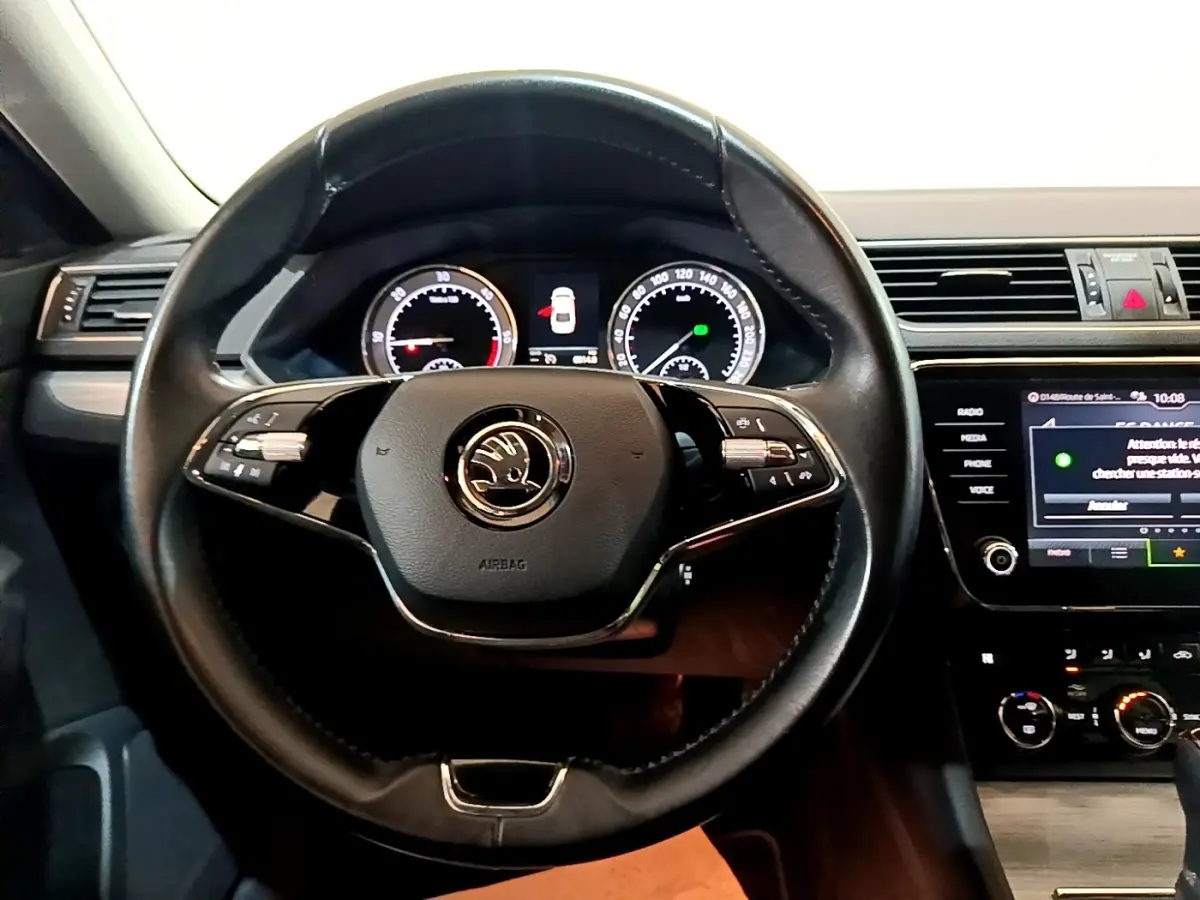 Vue intérieure centrée sur le volant cuir noir de la Skoda Superb 2.0 TDI 2021 avec tableau de bord digital et écran tactile.