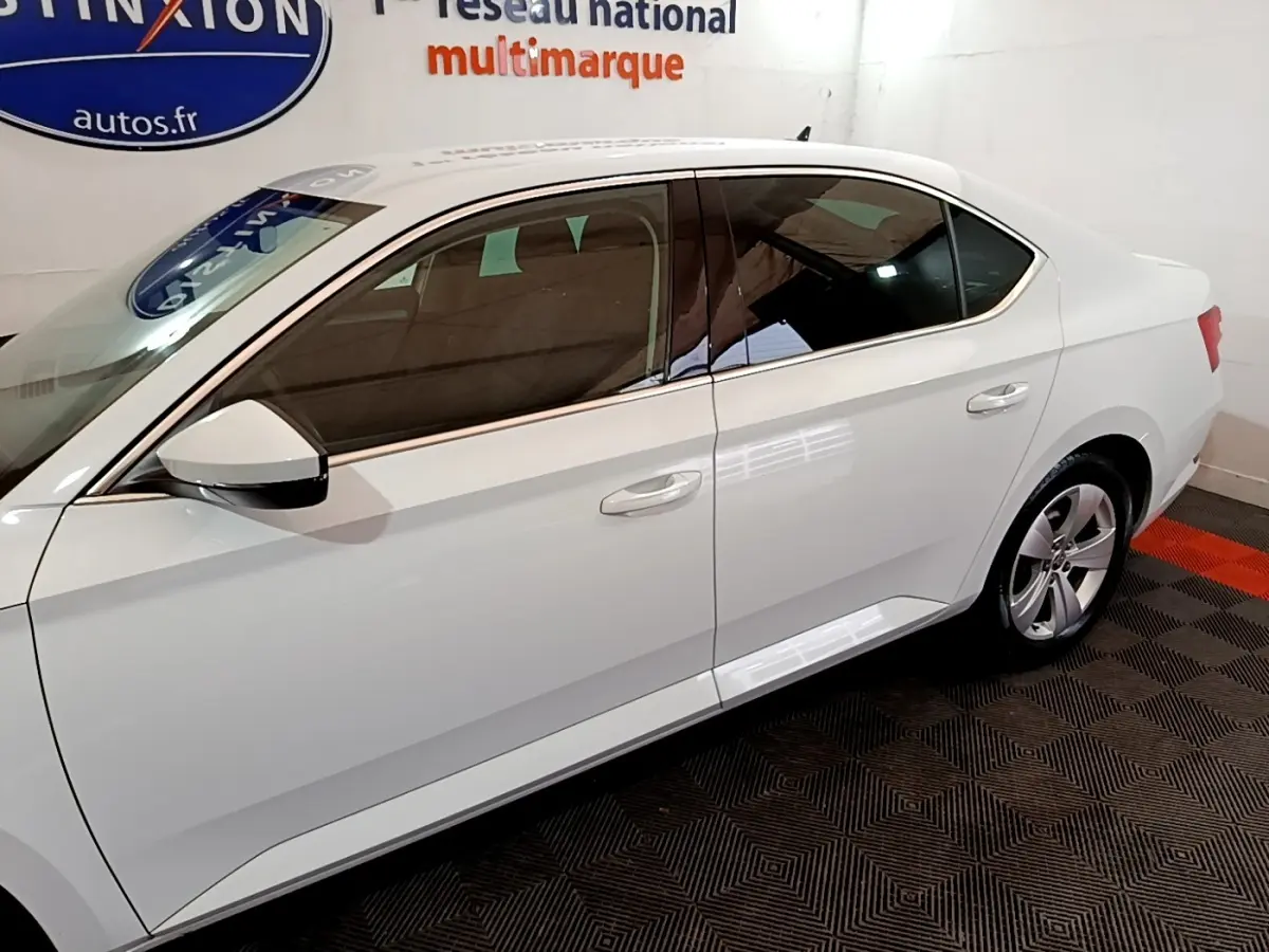 Vue latérale droite d'une Skoda Superb blanche 2021 dans un showroom avec jantes alliage et vitres teintées.