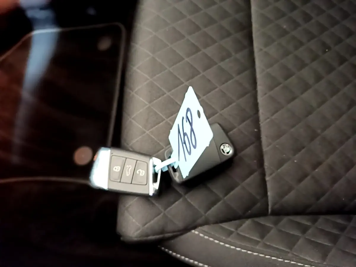 Gros plan sur la clé de voiture SKODA posée sur un siège intérieur noir matelassé avec étiquette numérotée.