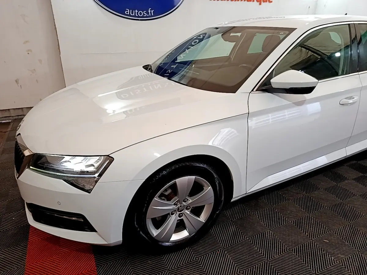 Vue 3/4 avant droit d'une Skoda Superb blanche avec phares LED et jantes alliage argentées.