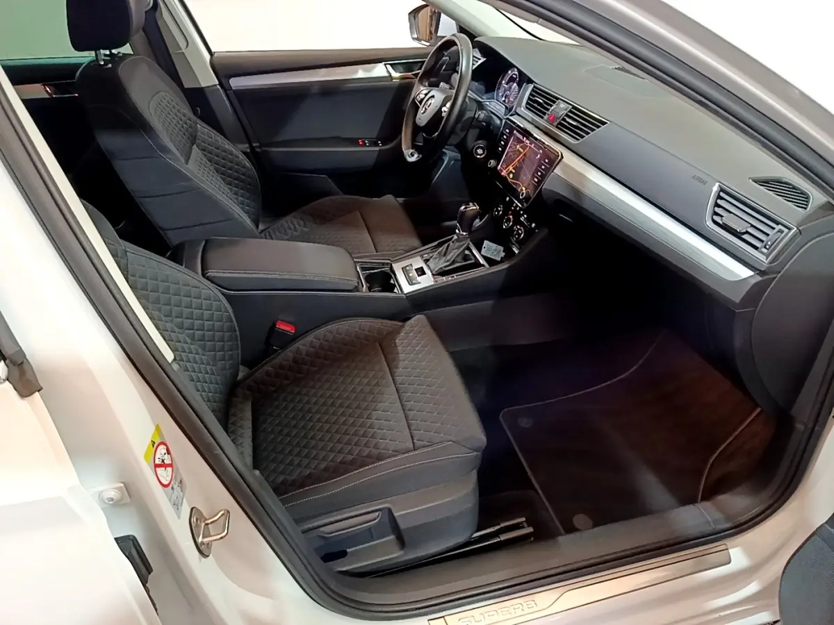 Intérieur côté conducteur d’une Skoda Superb blanche 2021, sièges noirs matelassés et tableau de bord avec écran tactile.
