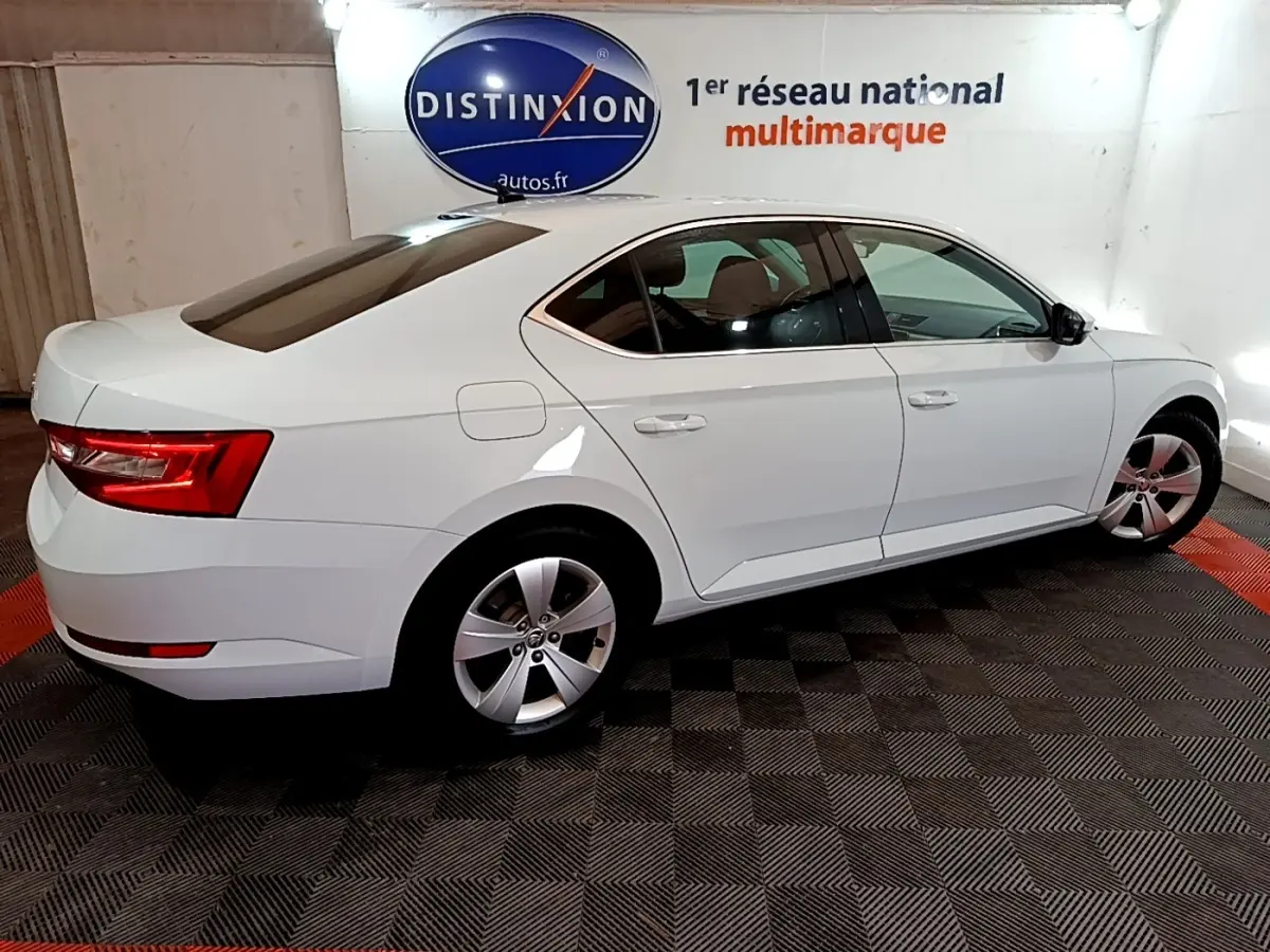 Vue de profil droit d’une Skoda Superb blanche 2.0 TDI Business en intérieur, avec jantes alliage et feux arrière LED.