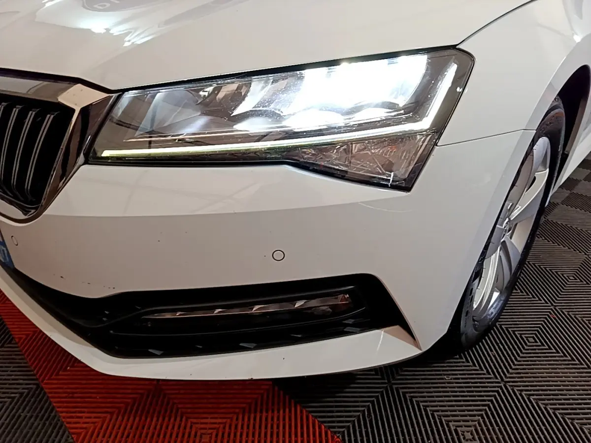 Gros plan sur l'avant droit blanc d'une Skoda Superb 2021, mettant en valeur le phare LED et la calandre noire.