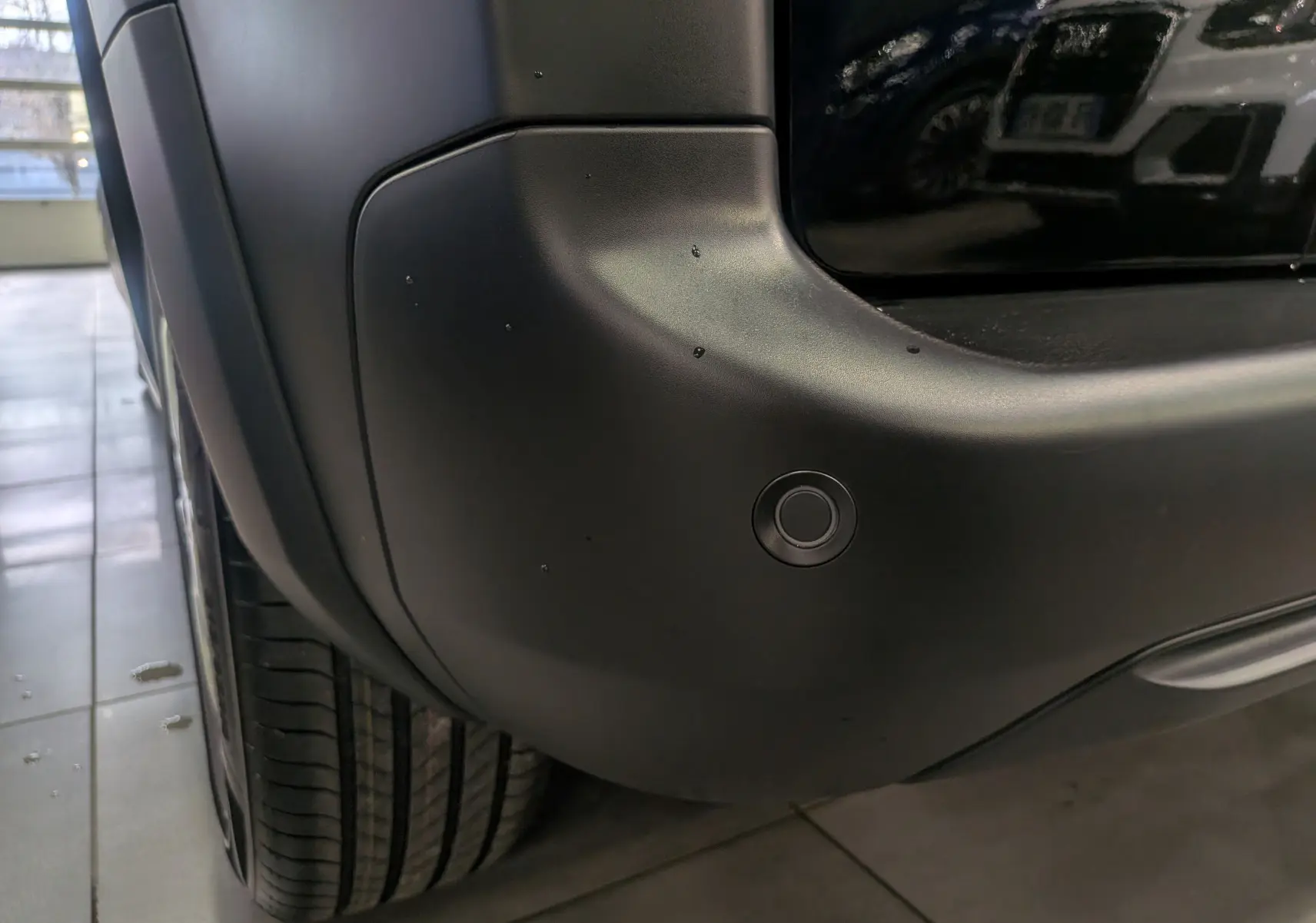 Gros plan sur le pare-chocs arrière droit noir du Peugeot Rifter 2025, avec capteur de stationnement visible.