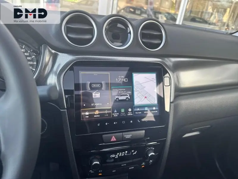 Vue intérieure du tableau de bord du Suzuki Vitara bleu, avec écran tactile multifonction et aérateurs ronds chromés.
