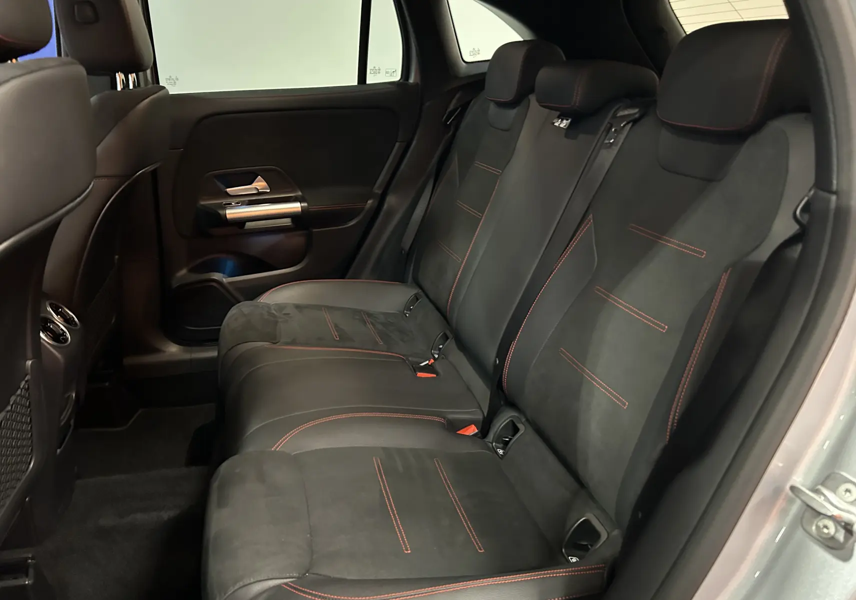 Vue intérieure arrière droite des sièges noirs avec surpiqûres rouges du Mercedes GLA 200 D AMG Line 2024 argent High-tech.