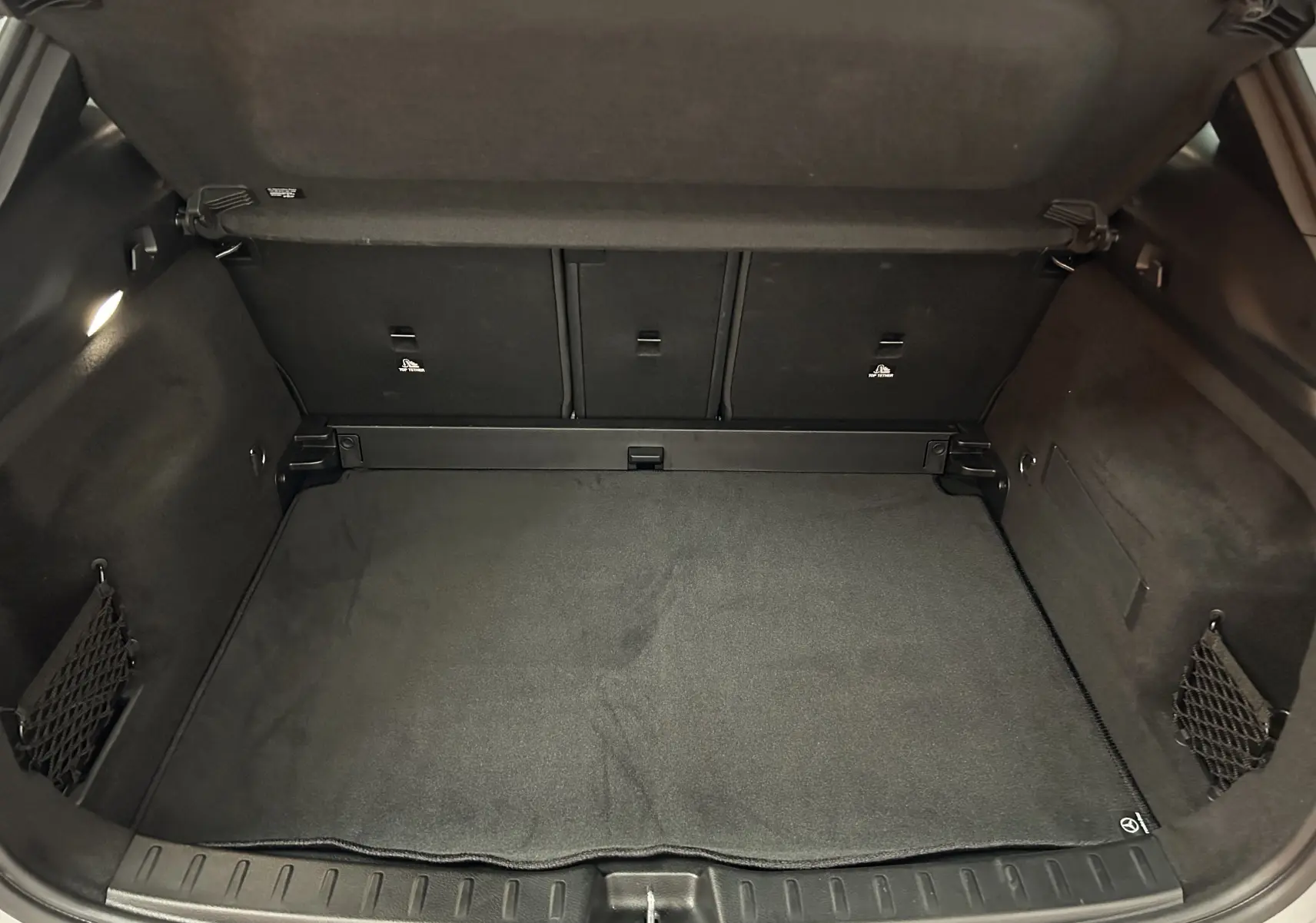 Coffre spacieux et noir du Mercedes GLA 200 D AMG Line 2024, avec tapis et filets latéraux visibles.