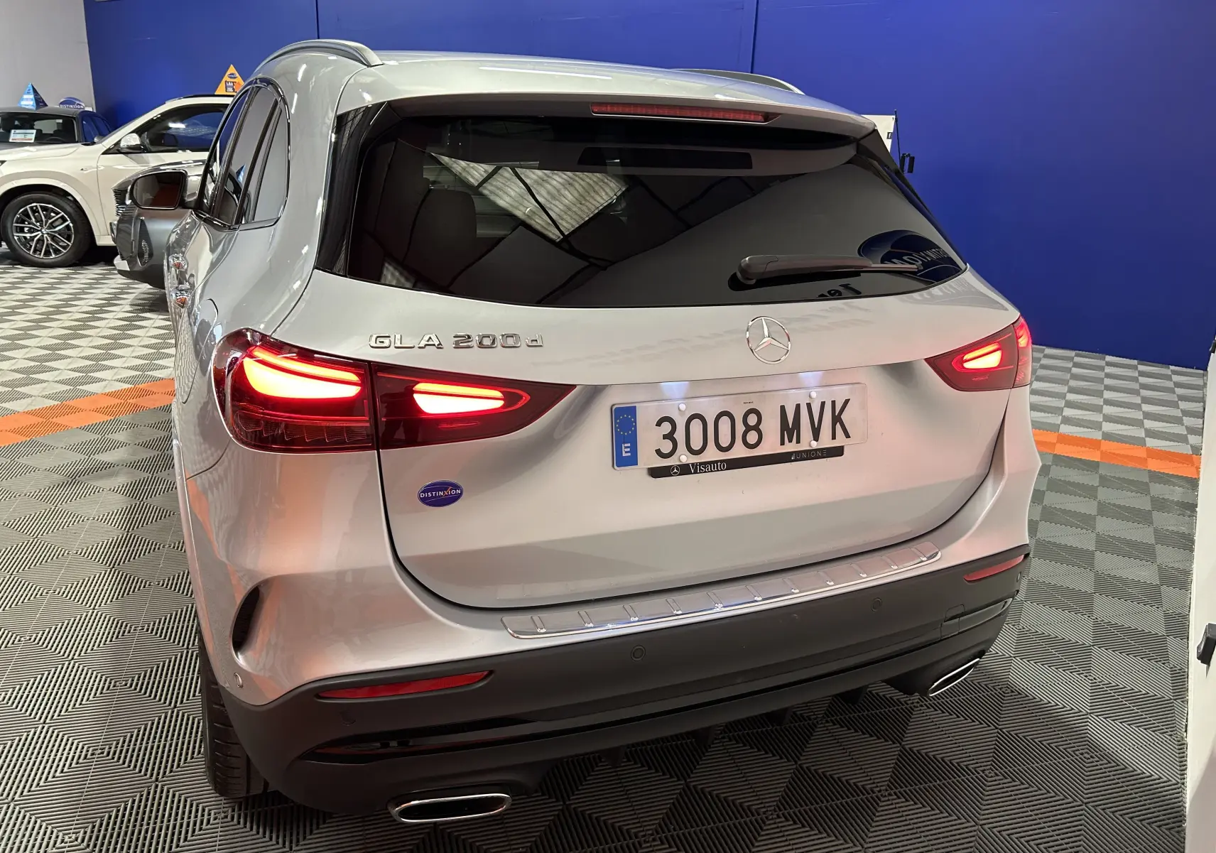 Vue 3/4 arrière d'un Mercedes GLA 200d argent High-tech avec feux allumés et vitres teintées foncées.