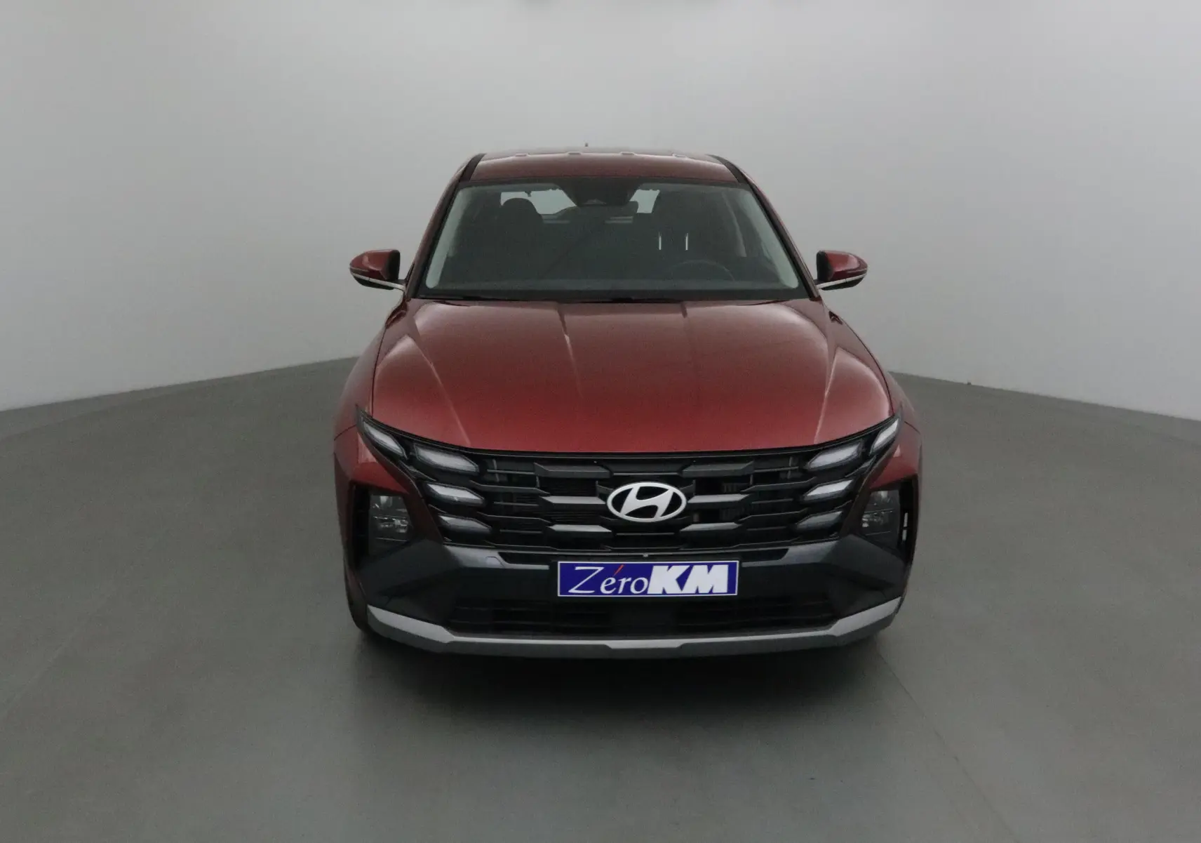 Vue frontale d'un Hyundai Tucson 2025 rouge Ultimate avec calandre noire et plaque Zero KM visible.