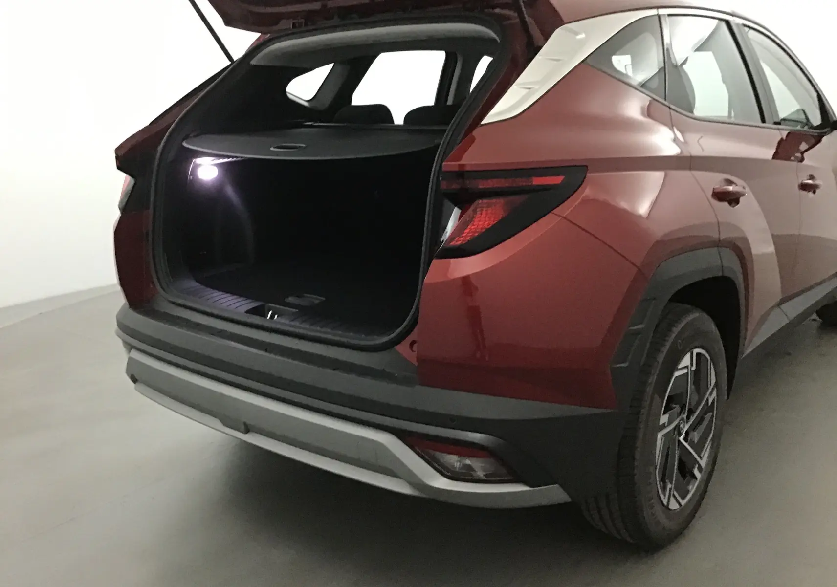 Vue arrière droite du Hyundai Tucson 2025 rouge Ultimate avec coffre ouvert et feux arrière allumés.