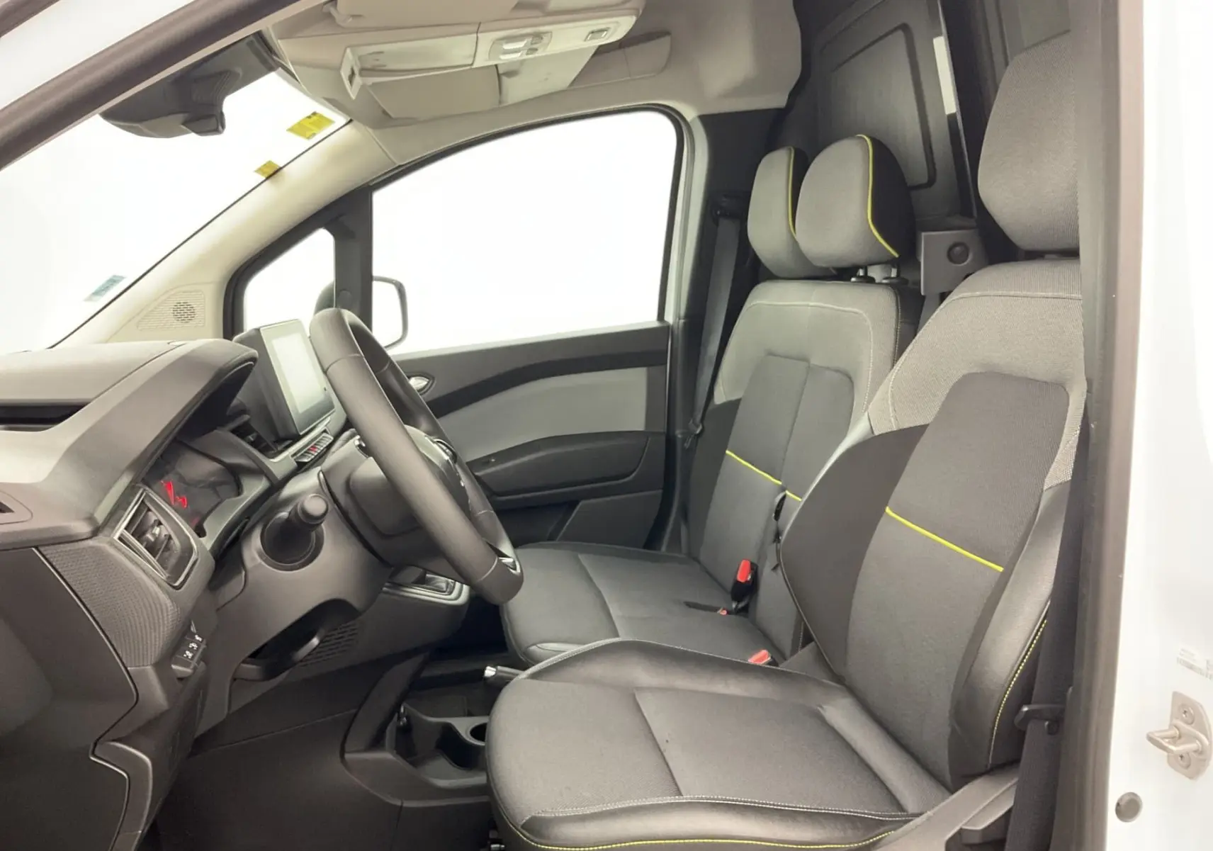 Vue intérieure côté conducteur du Renault Kangoo blanc 2024, sièges gris avec surpiqûres jaunes et tableau de bord moderne.