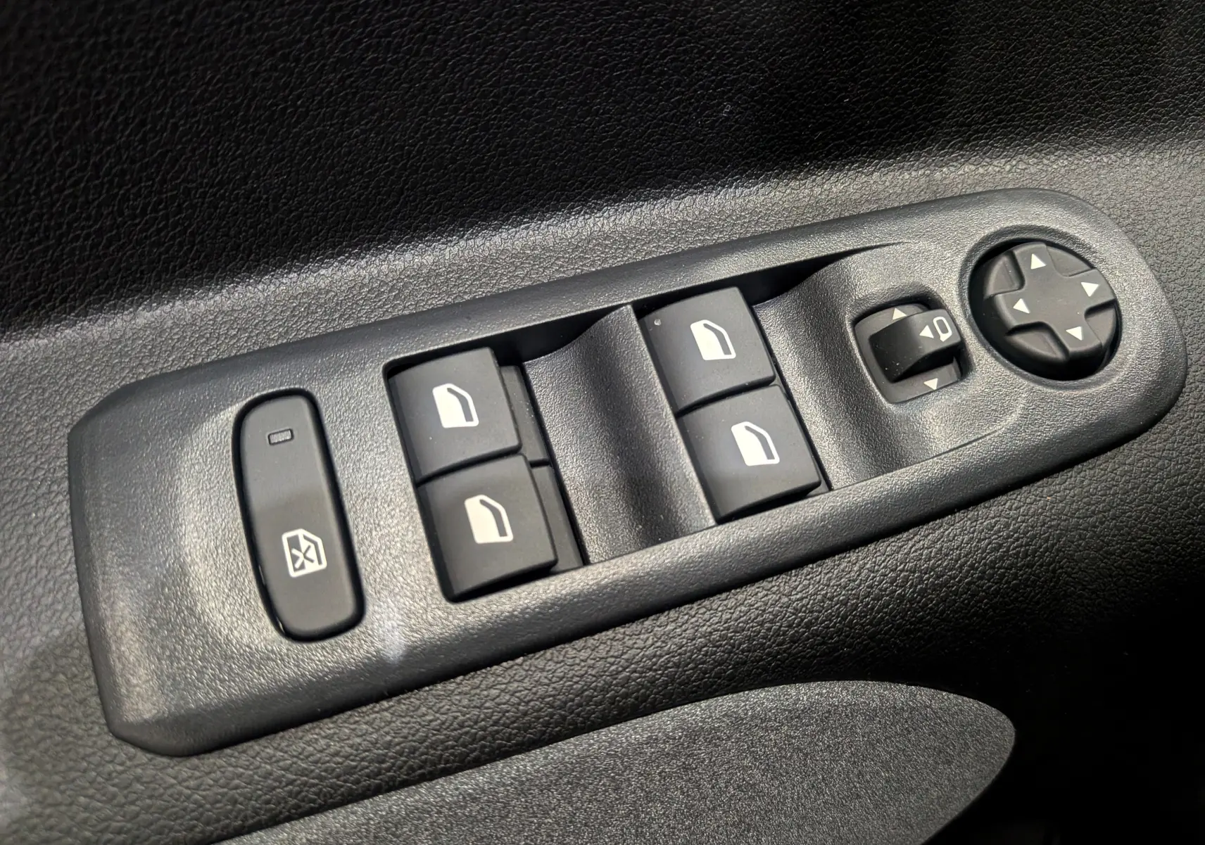 Gros plan sur les commandes de lève-vitres et réglage des rétroviseurs côté conducteur du Peugeot Rifter noir 2025.
