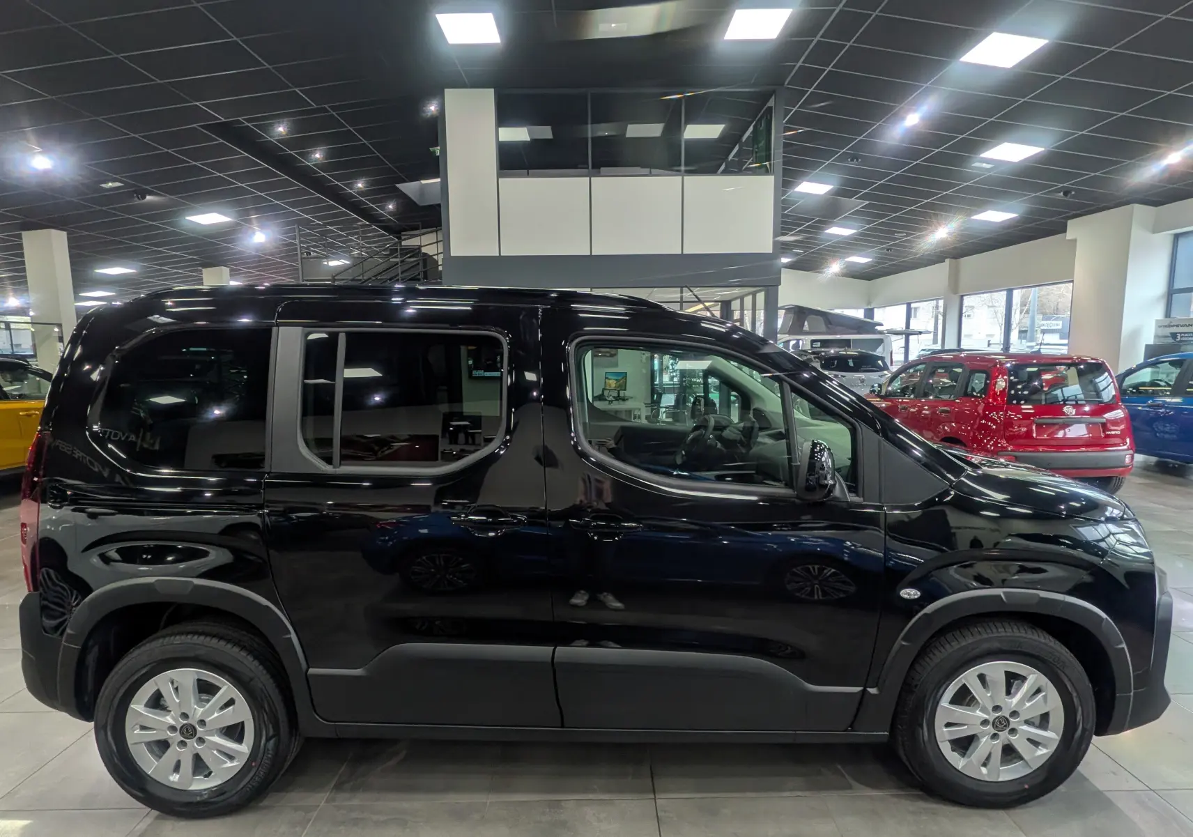 Vue de profil côté gauche d’un Peugeot Rifter noir 2025 en version M BlueHDi 130 S&S EAT8 5 places dans un showroom.